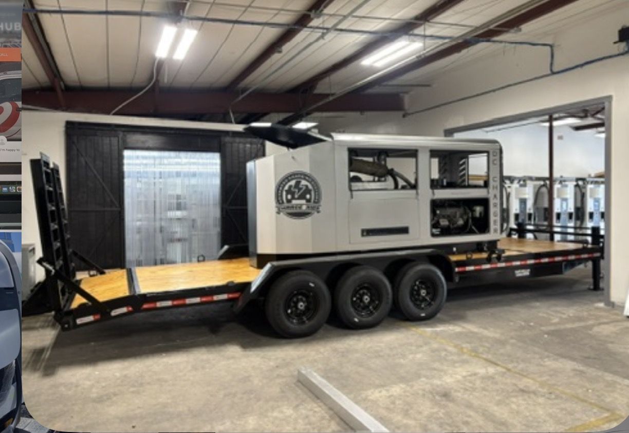 Trailer-mounted mobile DC fast charger on a triple-axle flatbed inside a workshop, with a row of DC dispensers behind it
