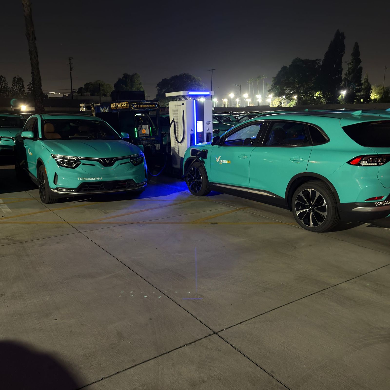 Rows of teal fleet SUVs in a depot at night with one vehicle plugged into a dual-port DC fast charger