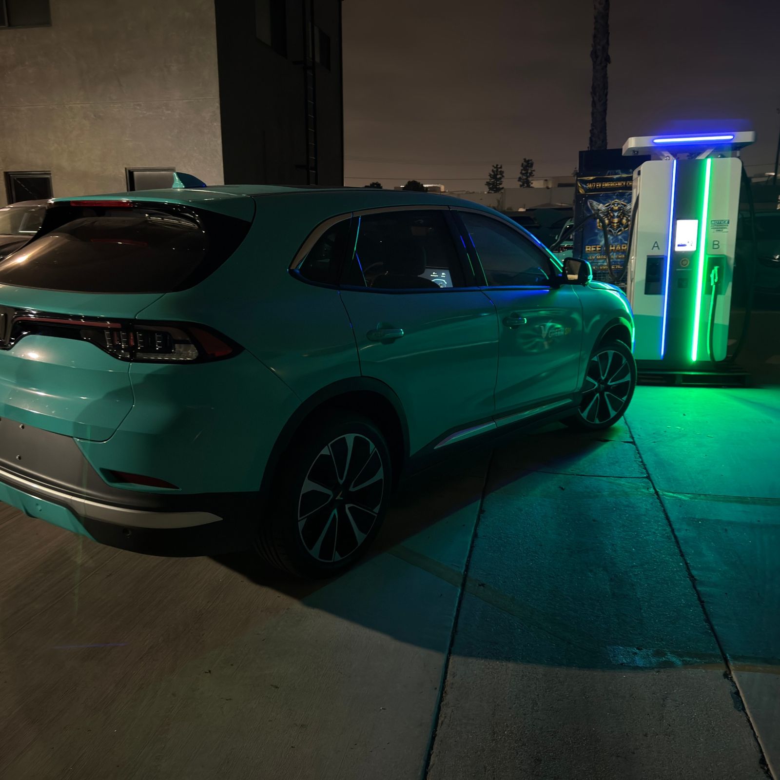 Teal fleet SUV parked at a dual-port DC fast charger lit blue and green at night