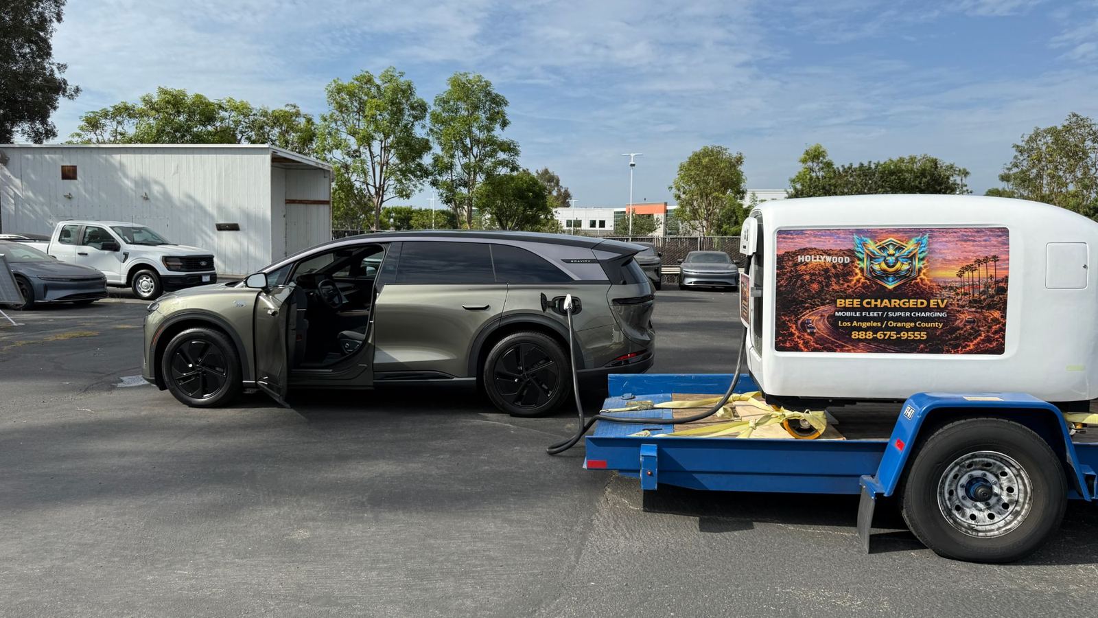Side view of a Lucid Gravity SUV charging from a trailer-mounted mobile DC pod in a vehicle lot
